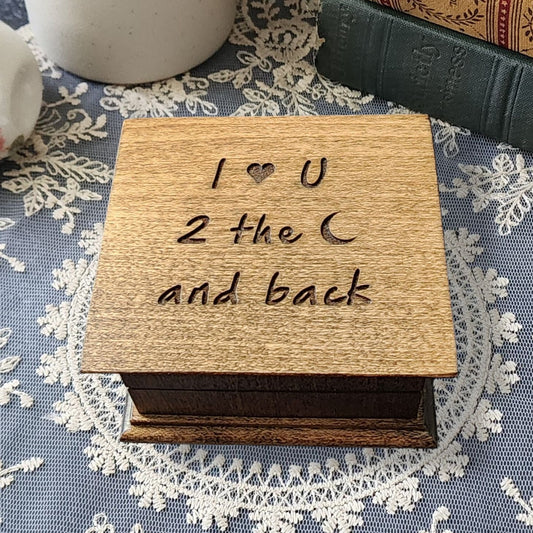 Wooden music box with 'I ❤️ U 2 the ❤️ and back' engraved on top on a lace tablecloth.