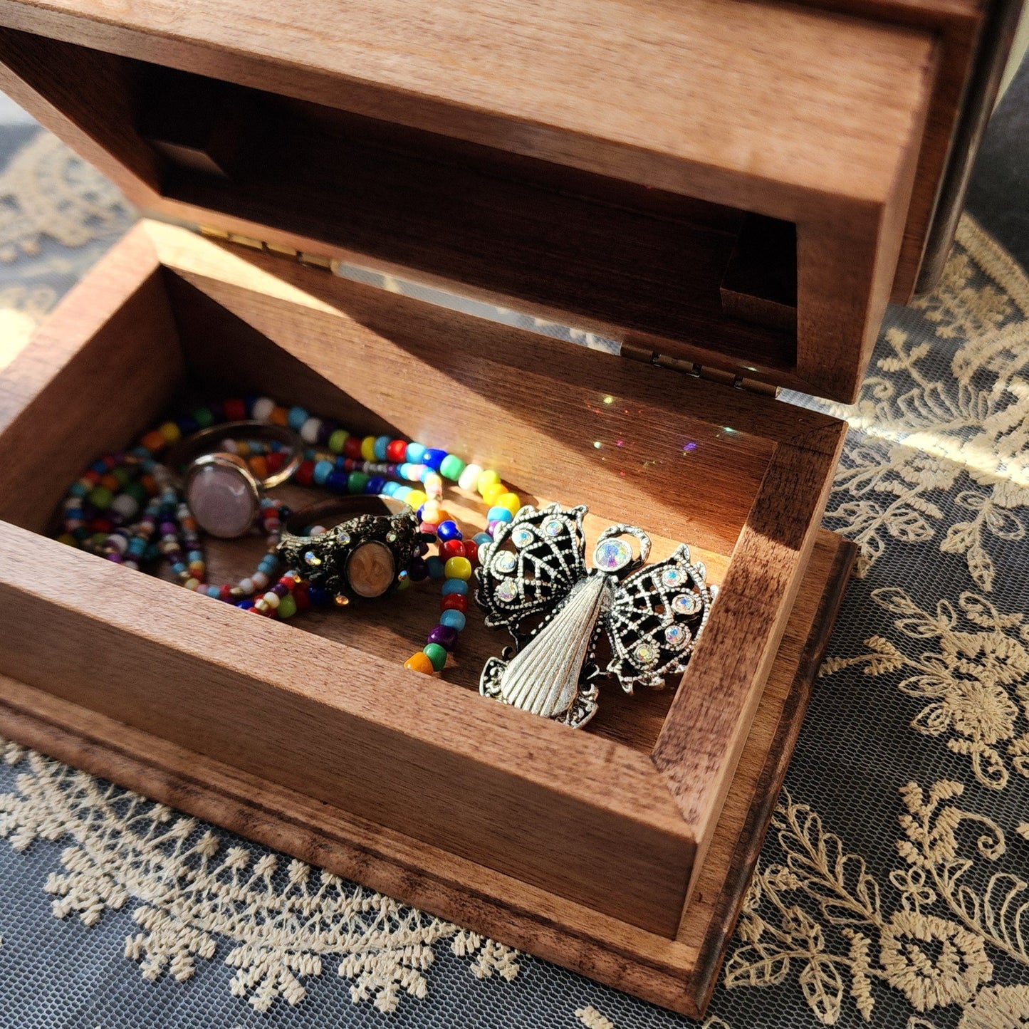 Wooden jewelry box with a colorful beaded necklace on a lace fabric background