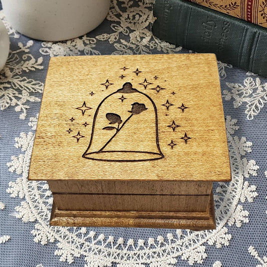 Small handcrafted wooden wind-up music box with engraved lid with rose under glass dome with stars surrounding it.