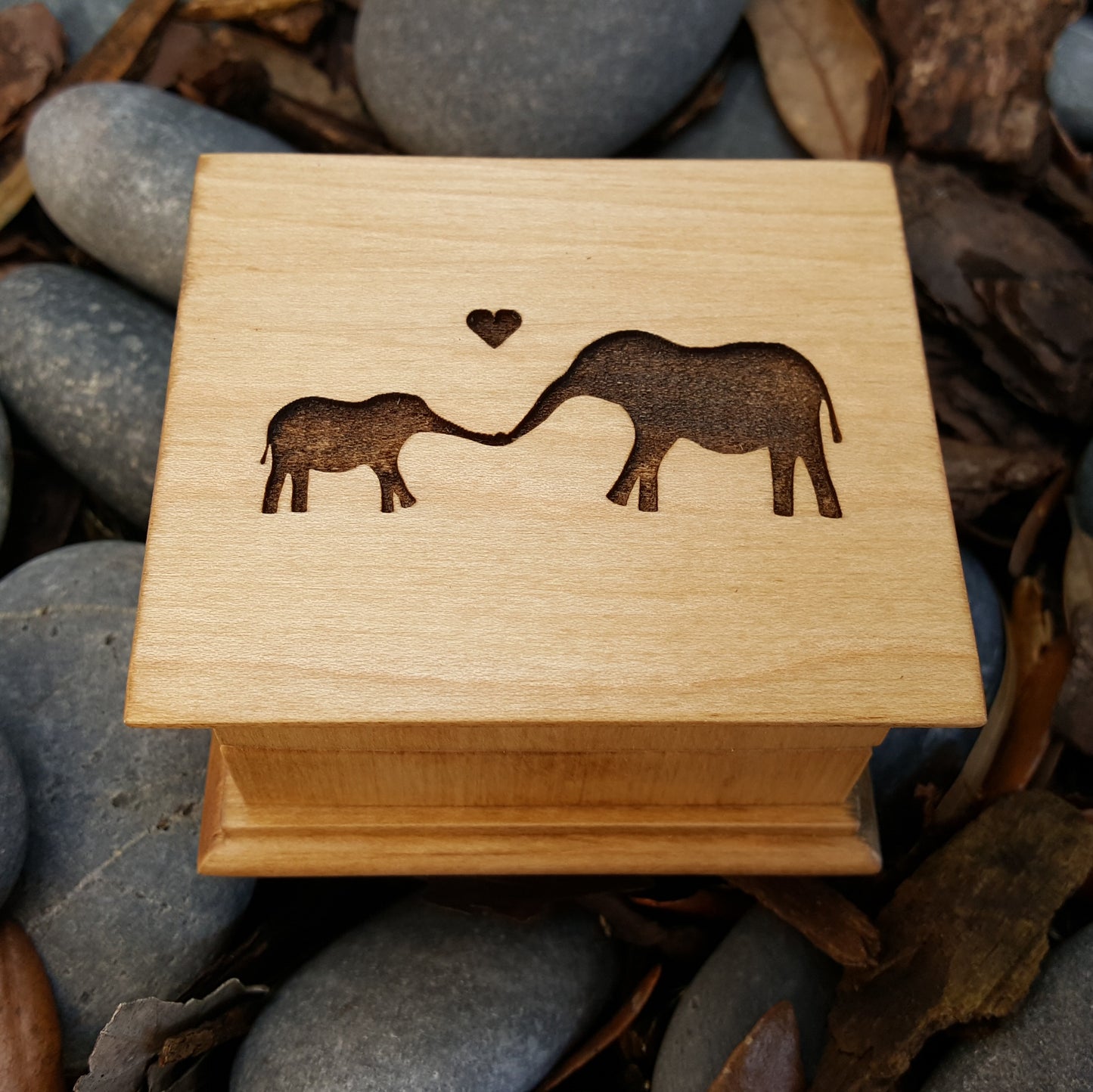 wooden music box in maple color, it has a baby and momma elephant engraved on top, choose song, color, add a personalized message to the bottom side of box