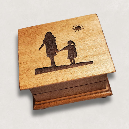 Wooden music box with engraved silhouette of mom and daughter holding hands and a sun on a light gray background