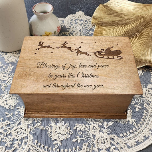 Wooden music box with Christmas message and a Santa Claus on his sleigh flying over the quote on a lace tablecloth with vases and leaves.