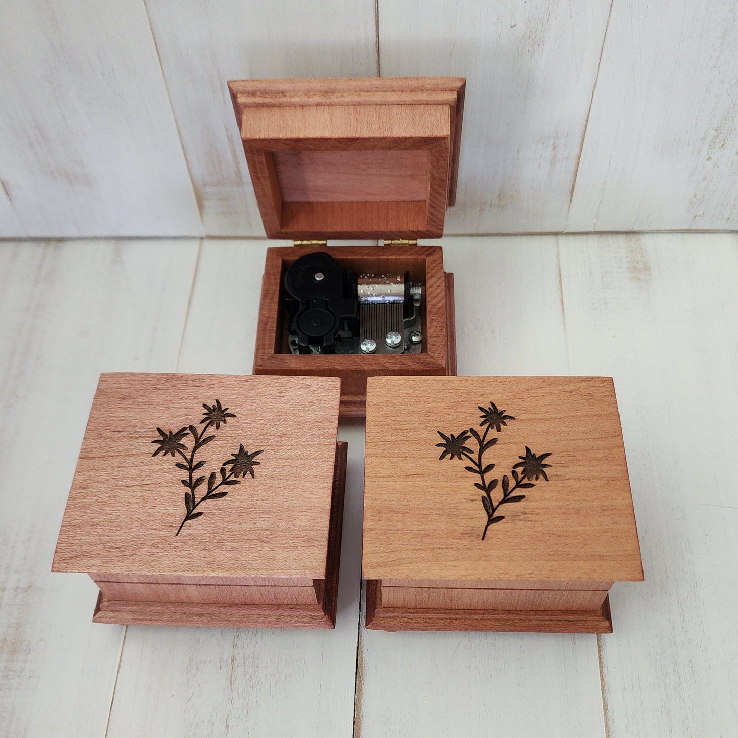wooden music boxes 3 pieces on a white washed wooden surface. 1 o the 3 is opened showing the 18 note music box mechanism