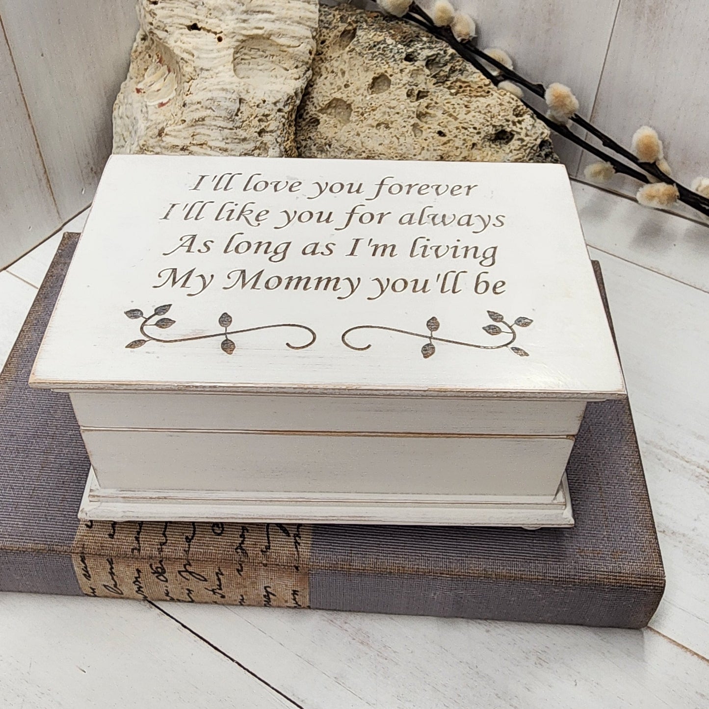 Handmade wooden music box engraved with the quote “I’ll love you forever, I’ll like you for always, as long as I’m living, my mommy you’ll be,” displayed on smooth river stones — sentimental personalized jewelry box for mom.
