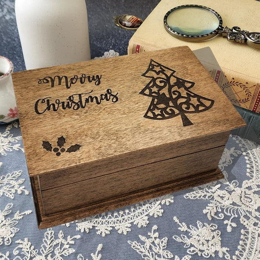 Wooden music box with 'Merry Christmas' and christmas tree design and a holy on a lace tablecloth.
