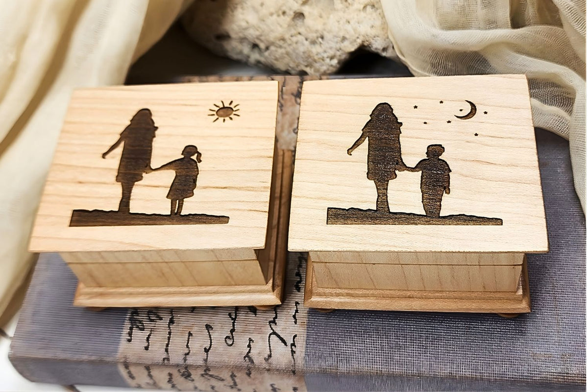 Two wooden music boxes with engraved silhouettes of mom and daughter design on one and mom and son on the other one