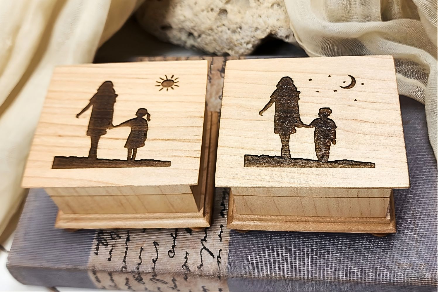 Two wooden music boxes with engraved silhouettes of mom and daughter design on one and mom and son on the other one