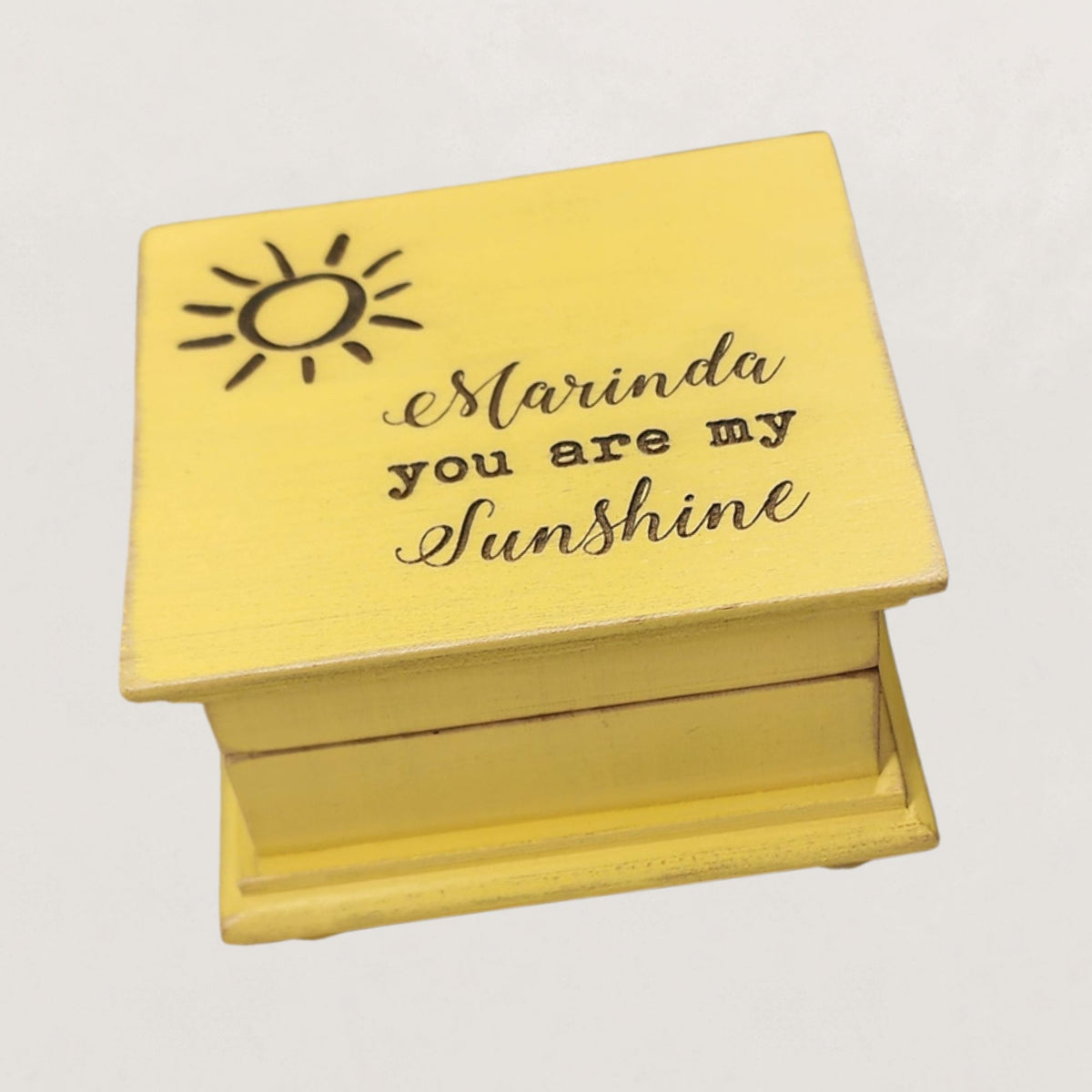 Yellow wooden music box with 'Marinda you are my sunshine' engraving on a light gray background