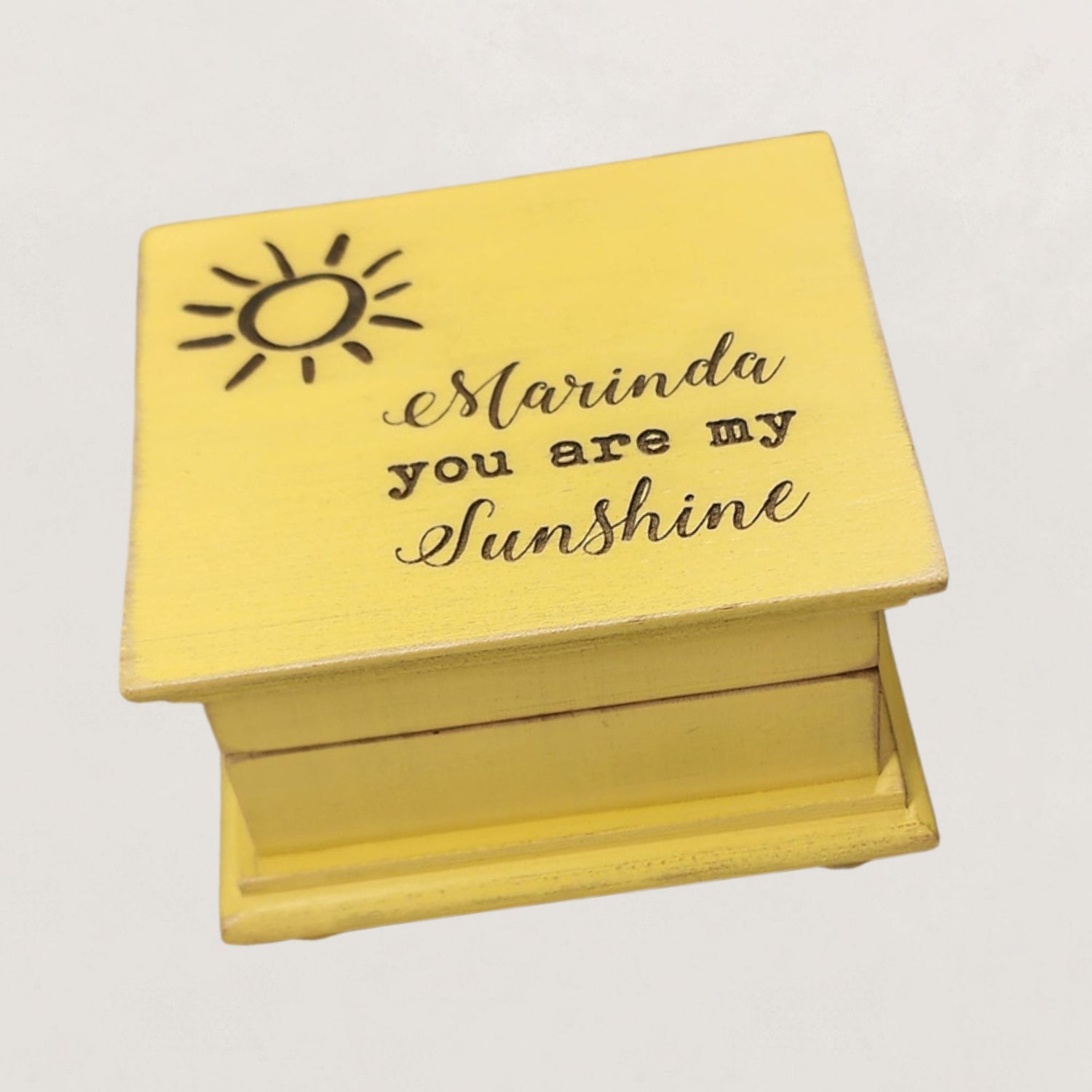Yellow wooden music box with 'Marinda you are my sunshine' engraving on a light gray background