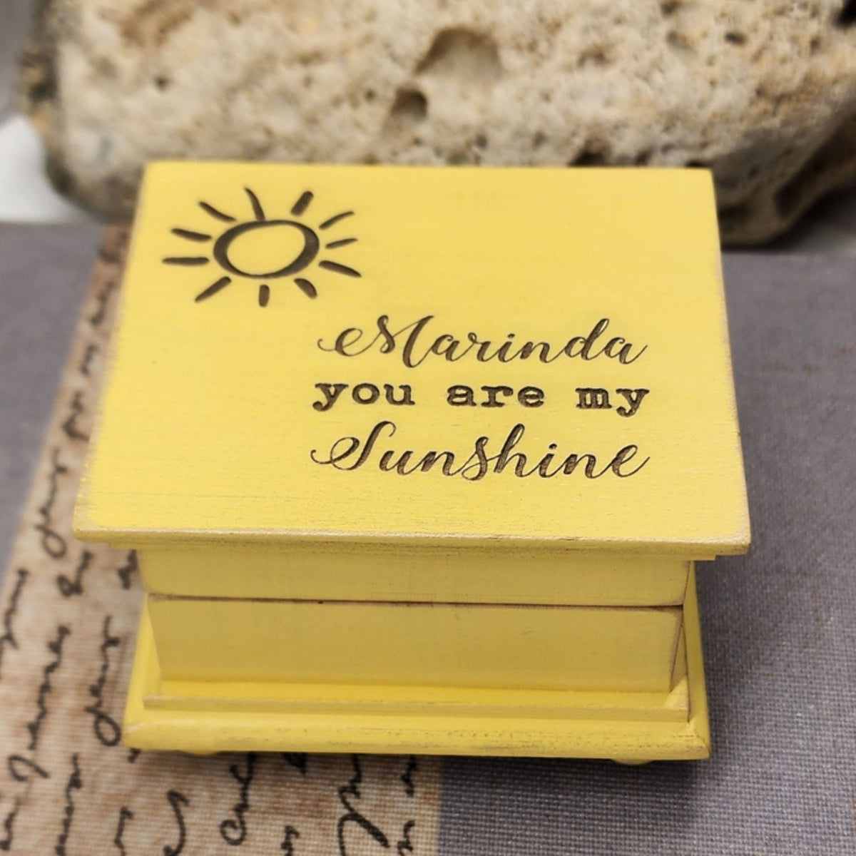 Vintage Yellow wooden music box with 'Marinda you are my sunshine' text and sun illustration on a textured surface.