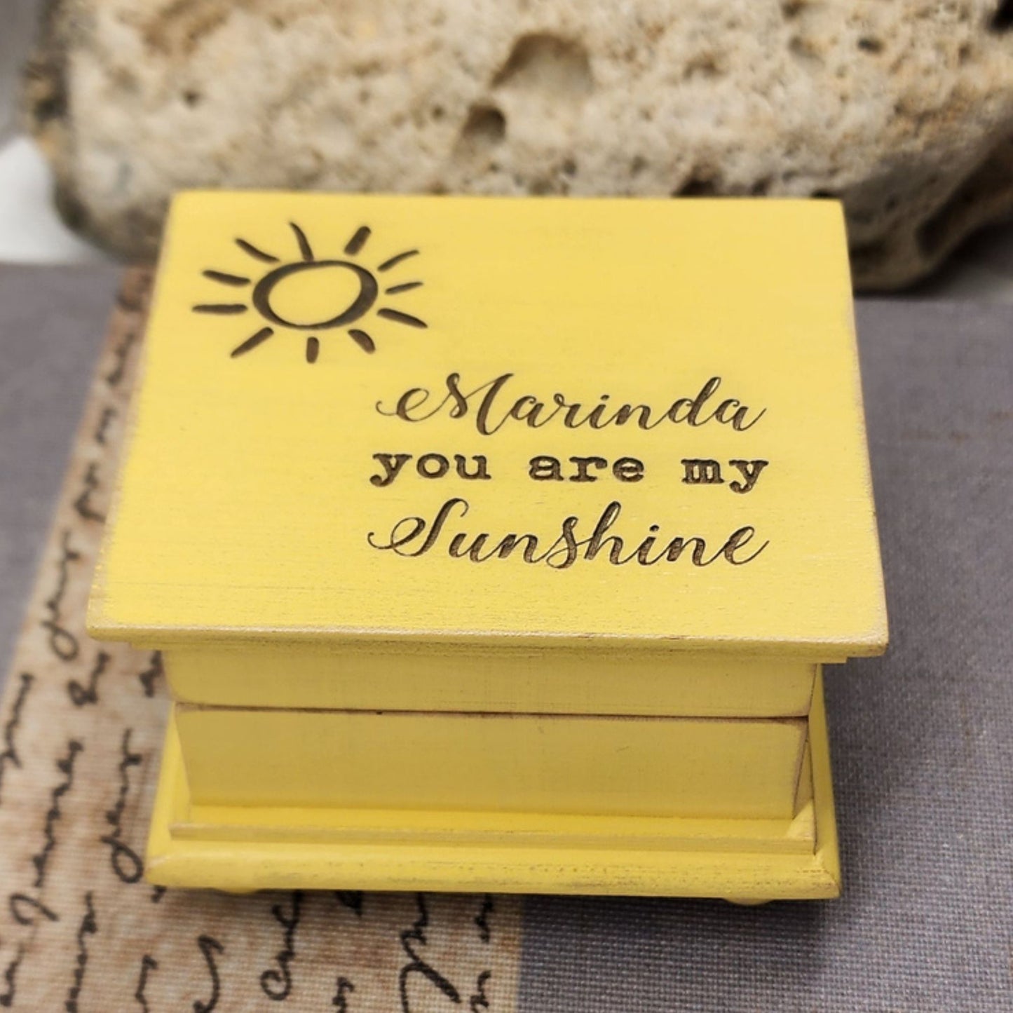 Vintage Yellow wooden music box with 'Marinda you are my sunshine' text and sun illustration on a textured surface.