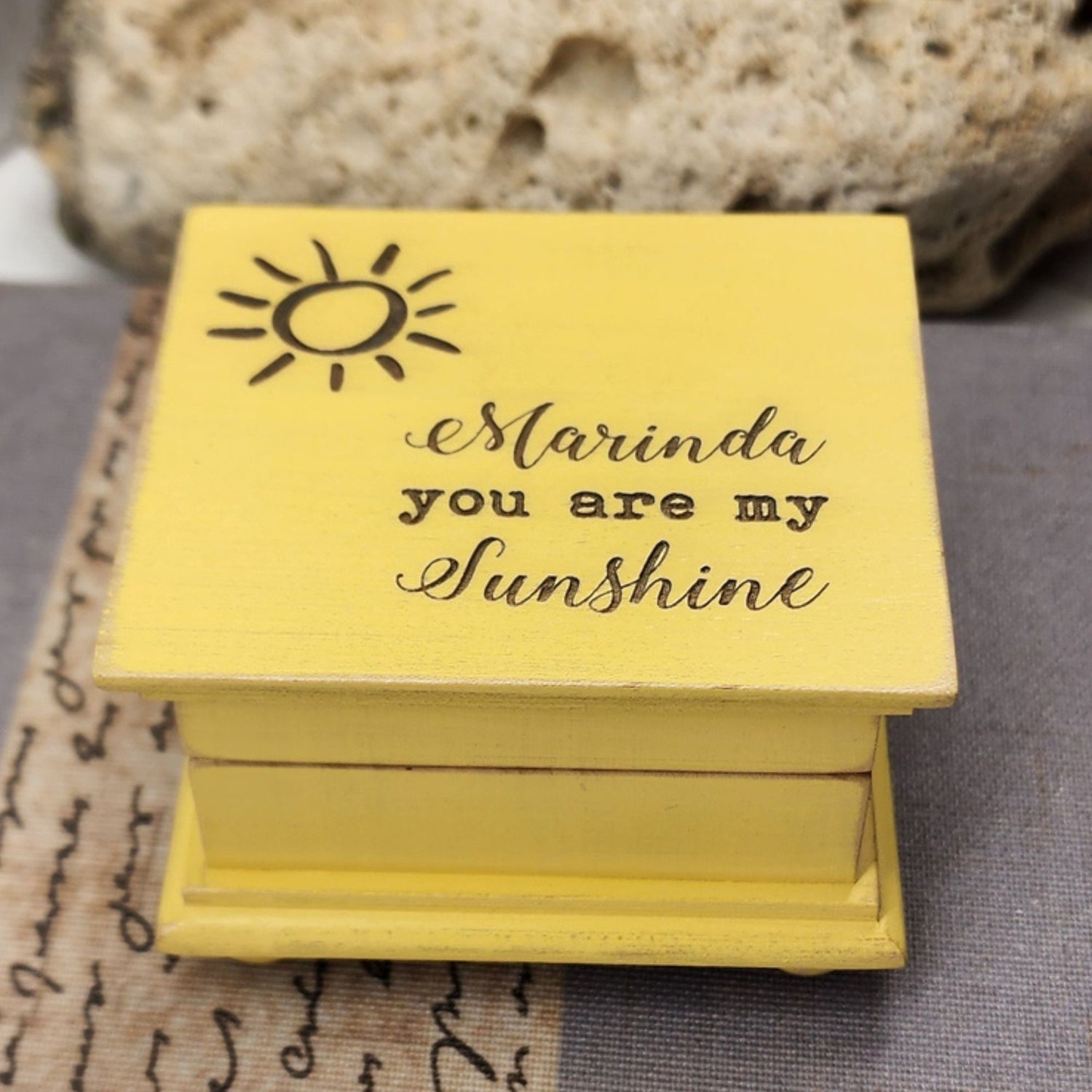 Vintage Yellow wooden music box with 'Marinda you are my sunshine' text and sun illustration on a textured surface.