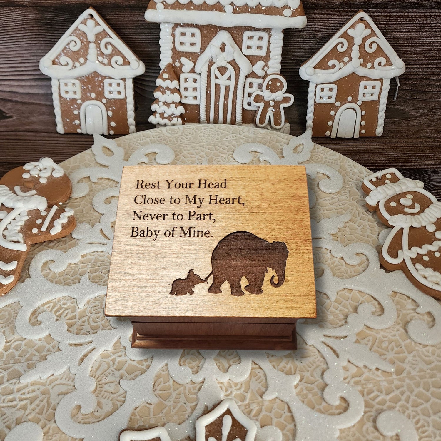 small wooden music box in chestnut with a momma and baby elephant silhouette engraved on the top along with the quote Rest Your Head Close to My Heart.... , choose the song Baby Mine and create a one-of-a-kind keepsake, it is photographed in a Christmas gingerbread setting