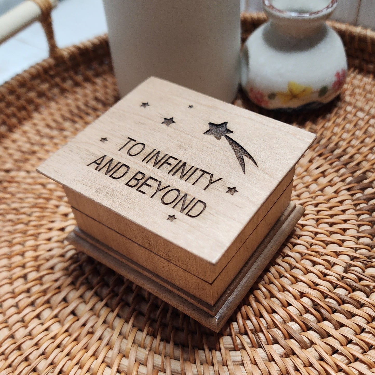 Small wooden music box with “To Infinity and Beyond” engraved on the lid, with stars and a shooting star, sitting on woven tray