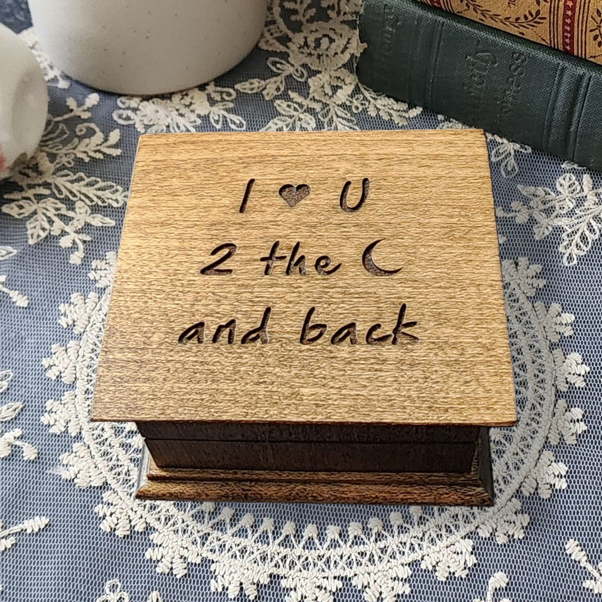 Wooden music box with 'I ❤️ U 2 the ❤️ and back' engraved on top on a lace tablecloth.