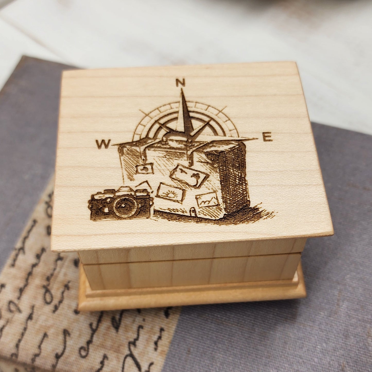 Wooden music box with engraved luggage, compass and camera design on a textured surface