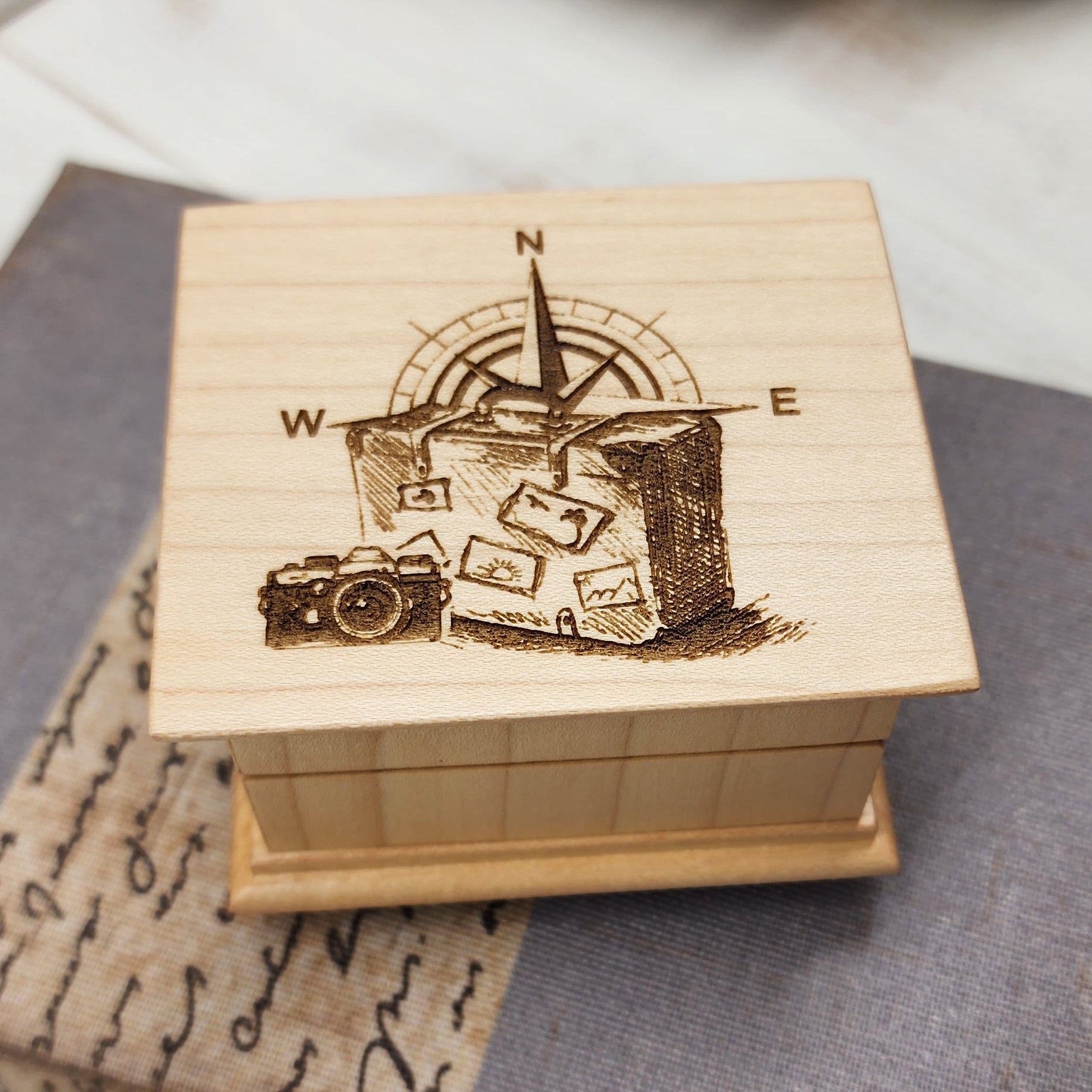 Wooden music box with engraved luggage, compass and camera design on a textured surface