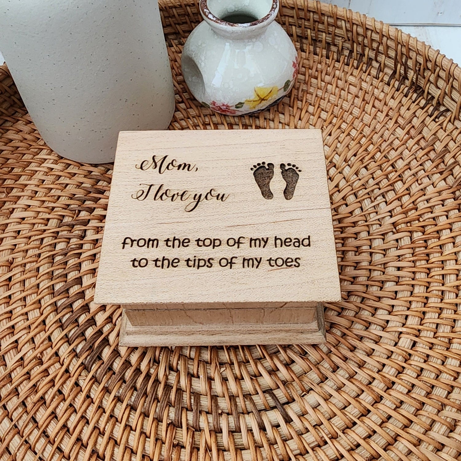 Small wooden music box with Mom I love you from the top of my head to the tips of my toes and footprints on a woven mat with a ceramic vase.