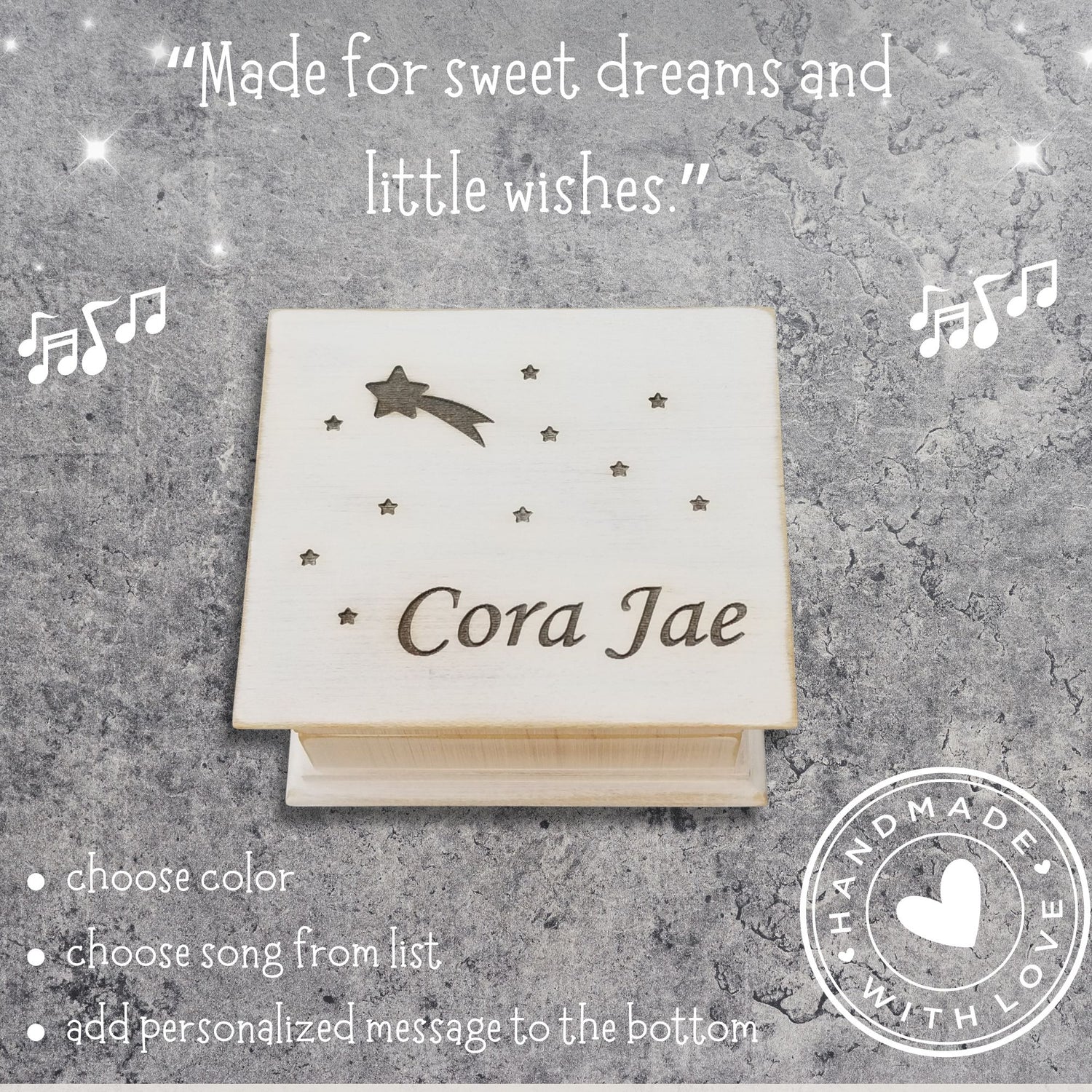 Wooden music box in vintage white with engraved name 'Cora Jae' on a textured gray background with decorative star and shooting star elements.