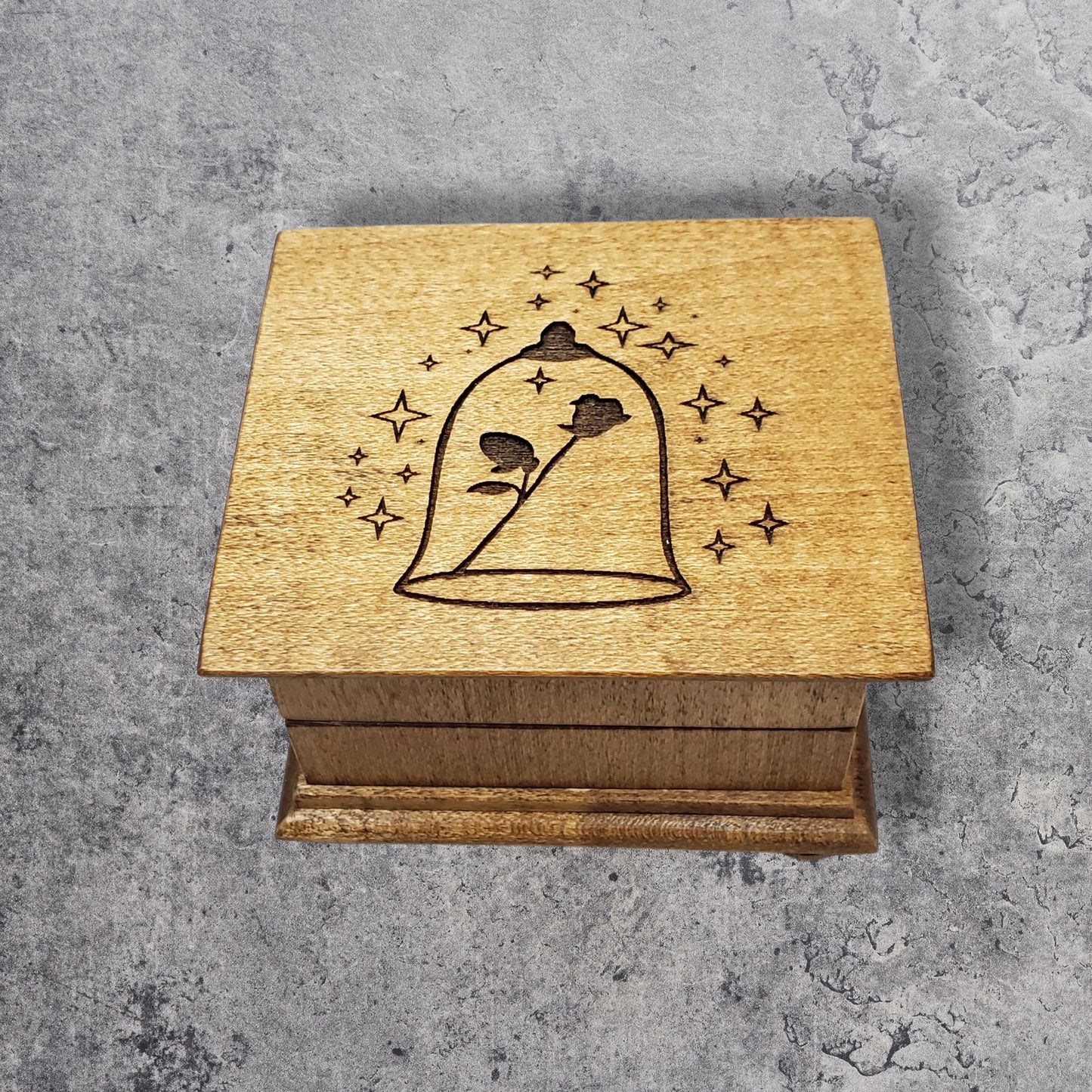 Small handcrafted wooden wind-up music box with engraved lid with rose under glass dome with stars surrounding it. 