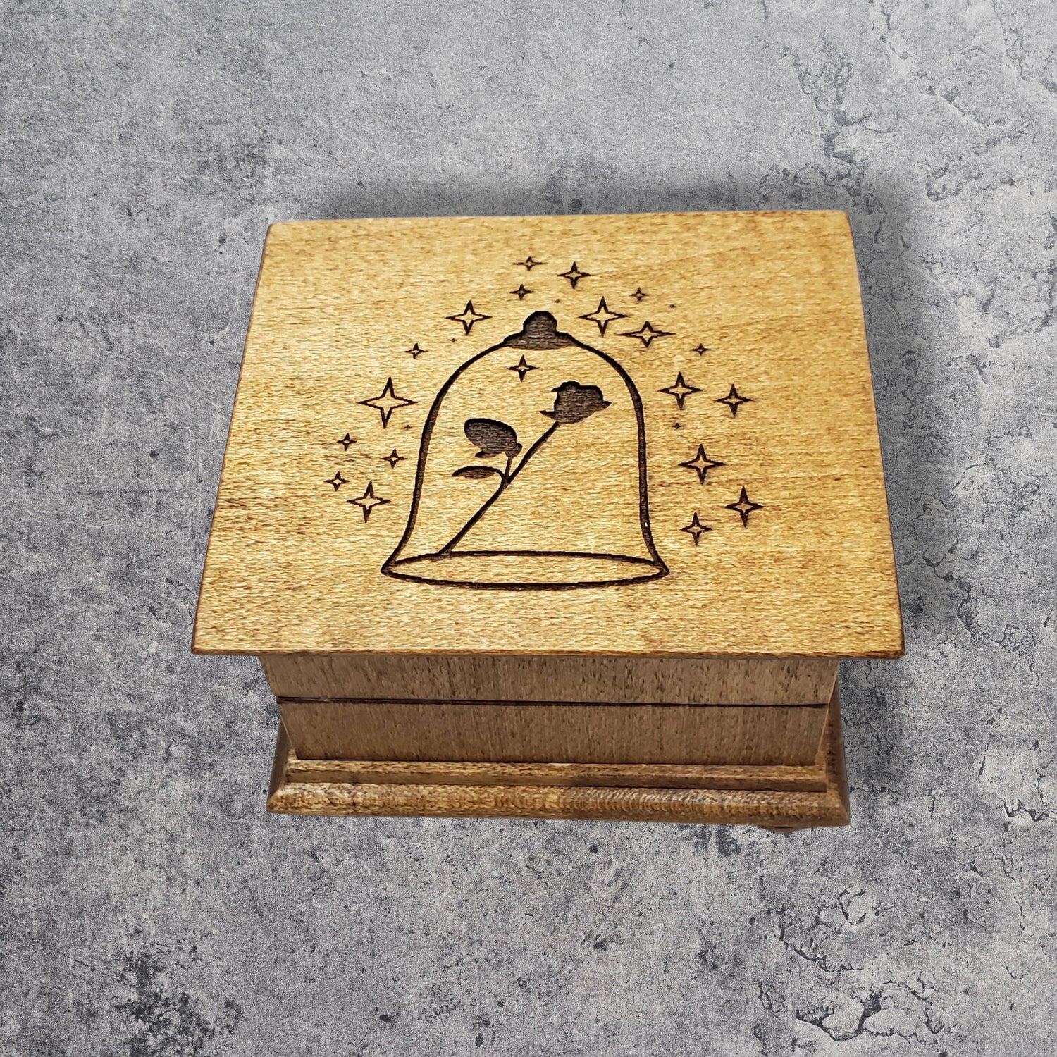 Small handcrafted wooden wind-up music box with engraved lid with rose under glass dome with stars surrounding it. 