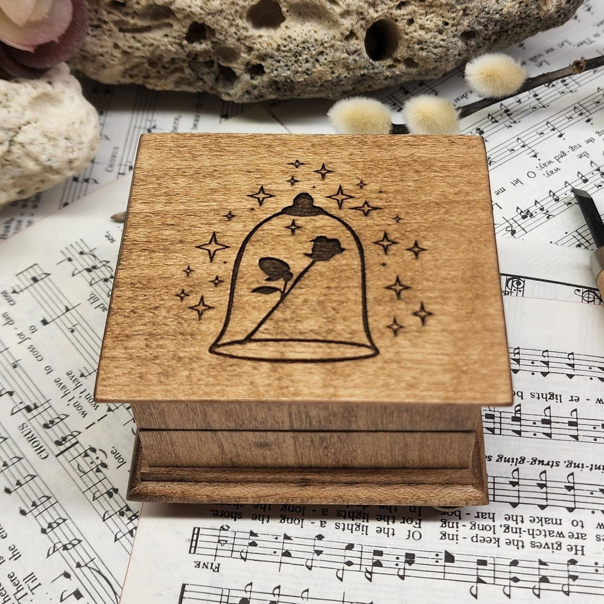 Small handcrafted wooden wind-up music box with engraved lid with rose under glass dome with stars surrounding it. 