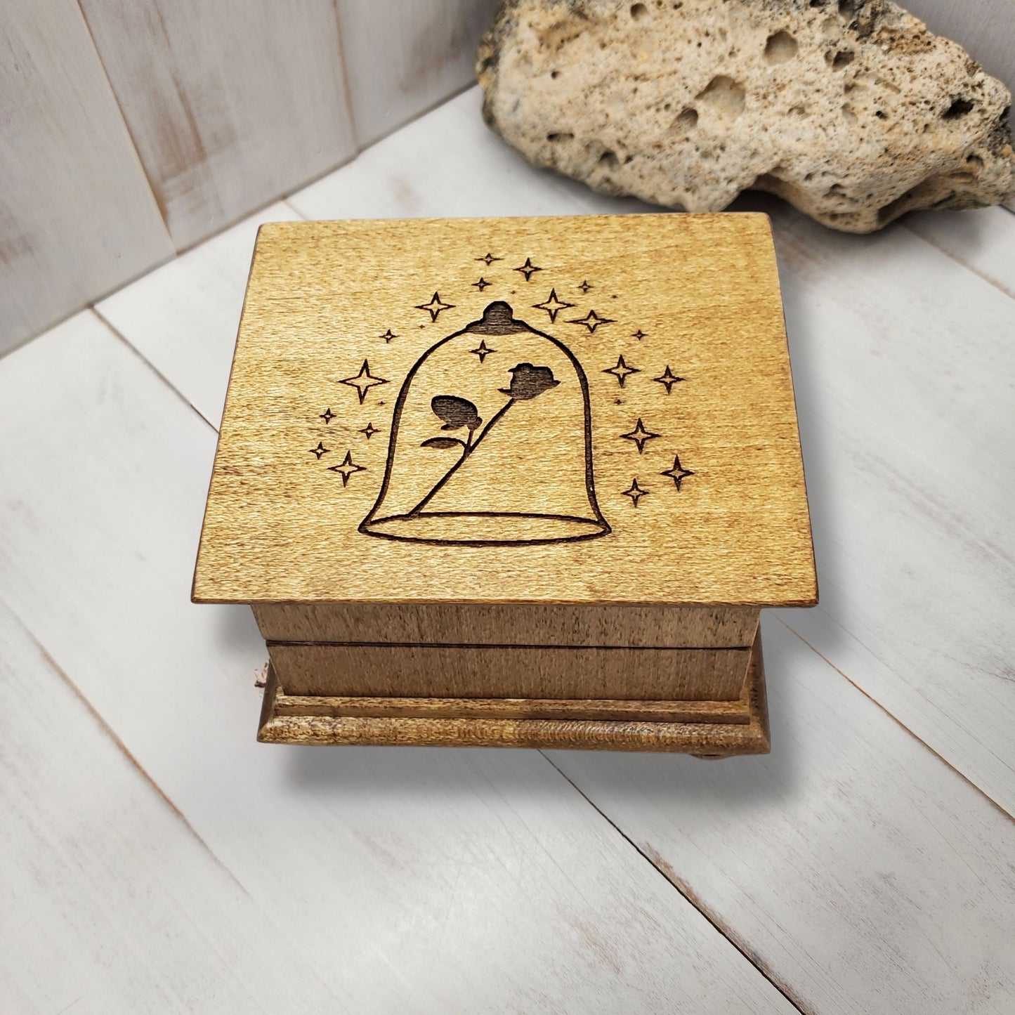 Small handcrafted wooden wind-up music box with engraved lid with rose under glass dome with stars surrounding it. 