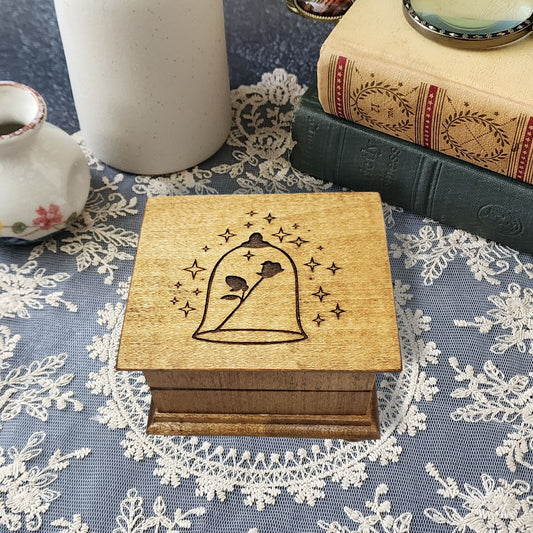 Small handcrafted wooden wind-up music box with engraved lid with rose under glass dome with stars surrounding it. 