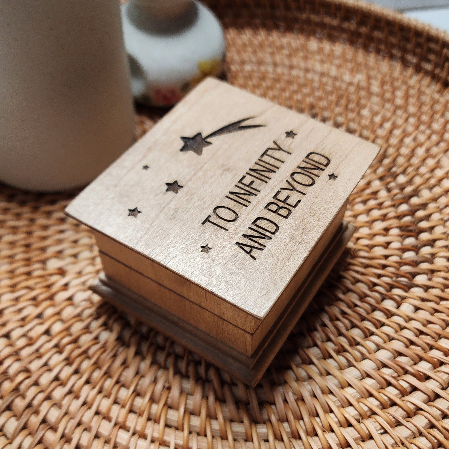 Small wooden music box with “To Infinity and Beyond” engraved on the lid, with stars and a shooting star, sitting on woven tray