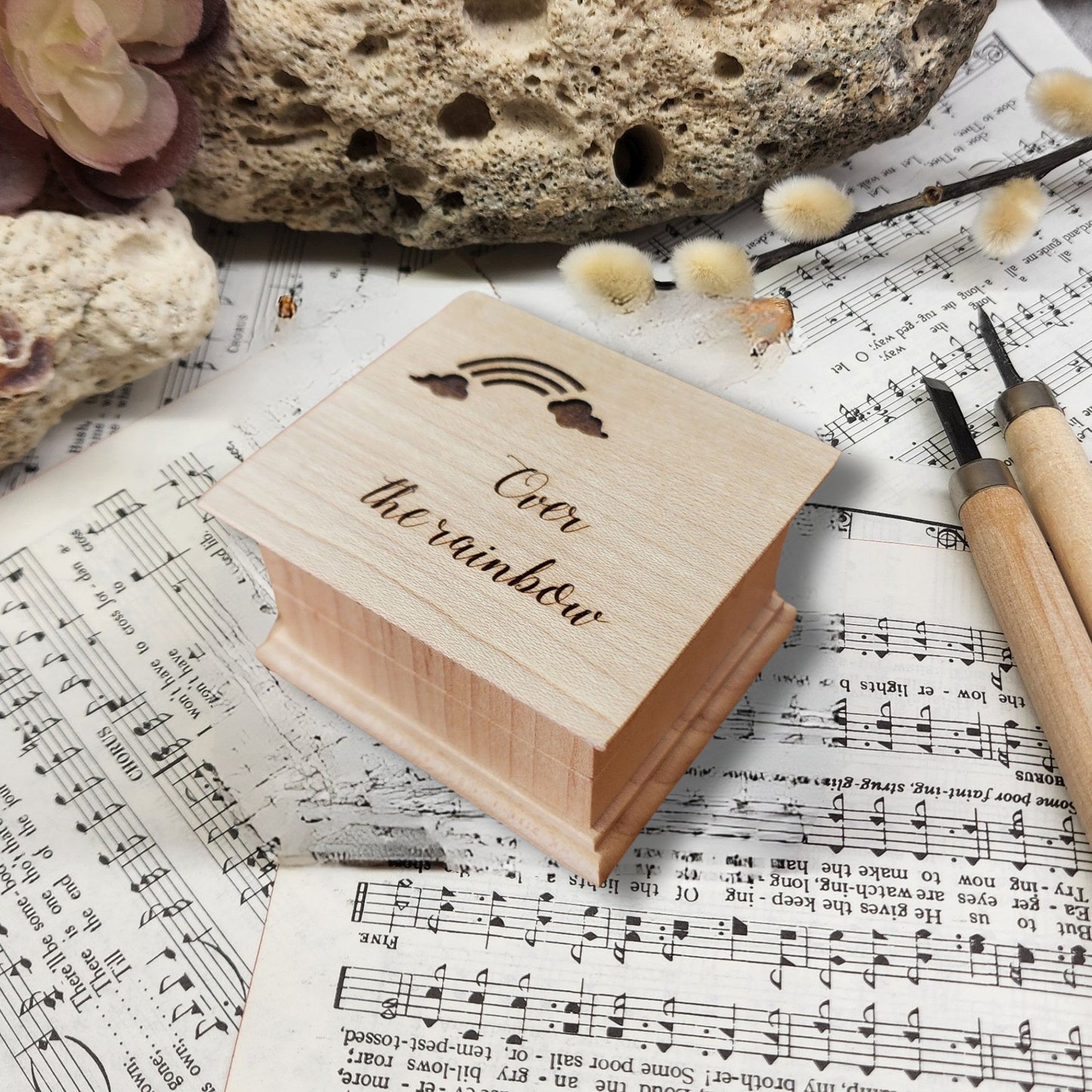 Wooden music box with 'Over the rainbow' engraving on sheet music with a rock and flowers.