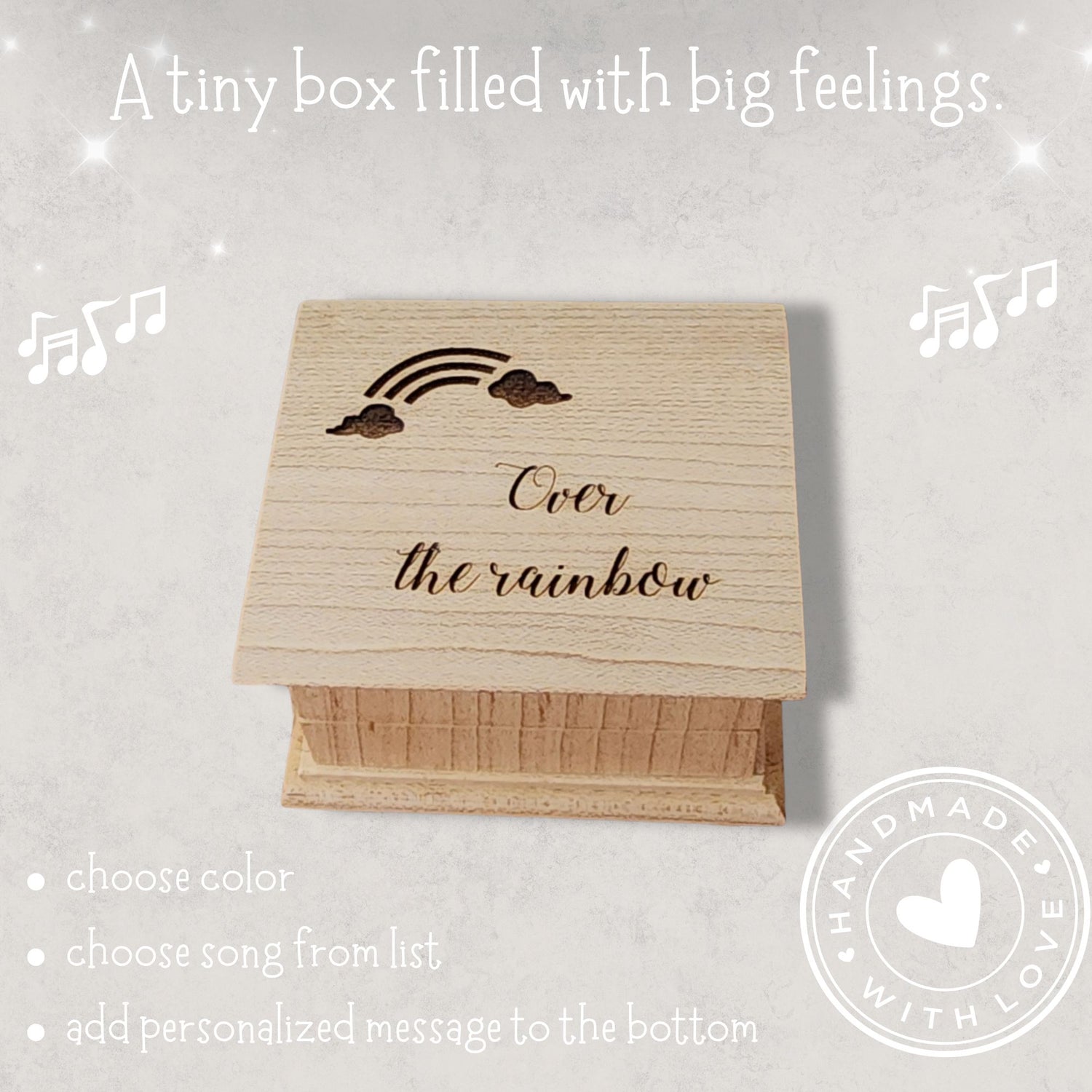 Wooden music box with 'Over the rainbow' text and rainbow with cloud design on a light gray background. With a handmade with love sticker in the corner of the image along with the quote: "A tiny box filled with big feelings"