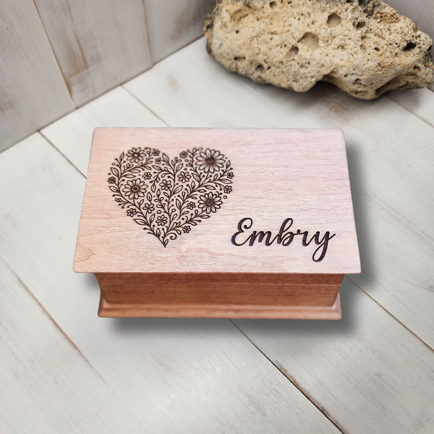 Wooden jewelry box with floral heart design and name engraving on a light wooden surface.