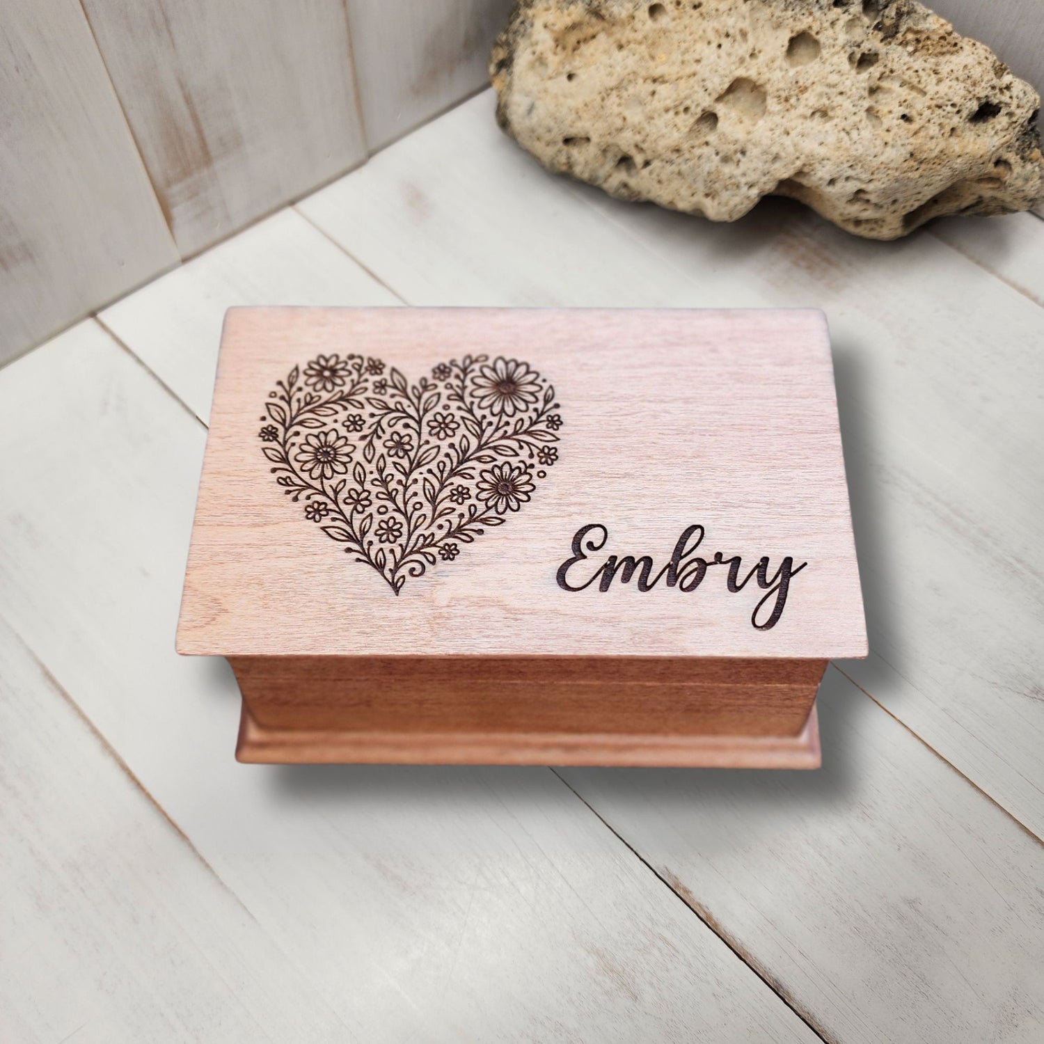 Wooden jewelry box with floral heart design and name engraving on a light wooden surface.