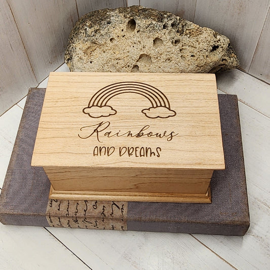 wooden jewelry box with a rainbow and clouds engraved on top with the words Rainbows and Dreams in a cute font