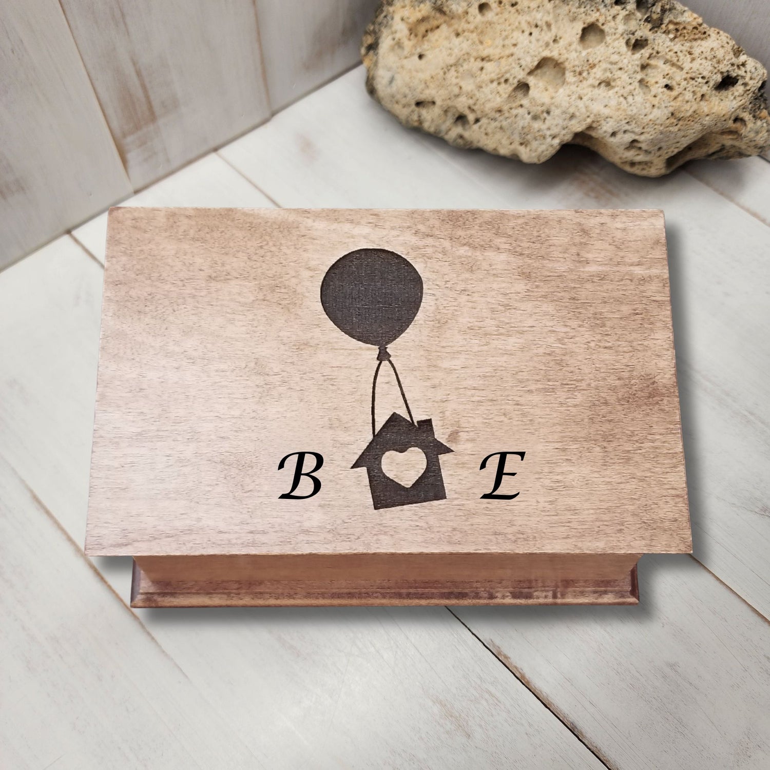 Personalized jewelry box with 'B E' and house with balloon design on a light wooden surface.