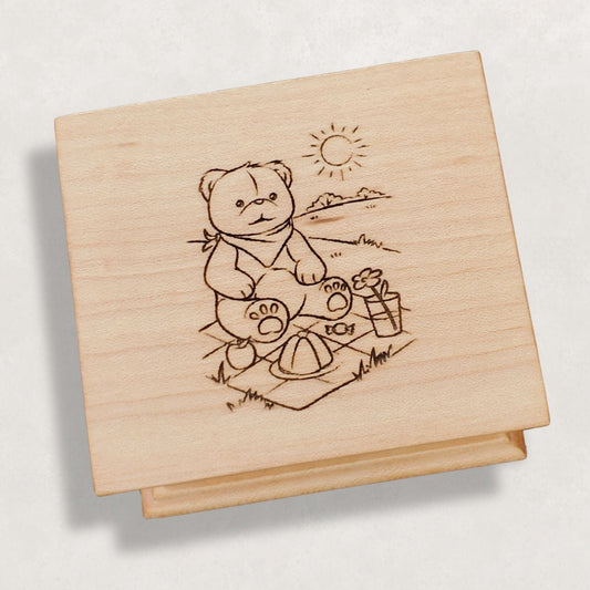 Wooden music box with a engraved illustration of a bear having a picnic on a light gray background