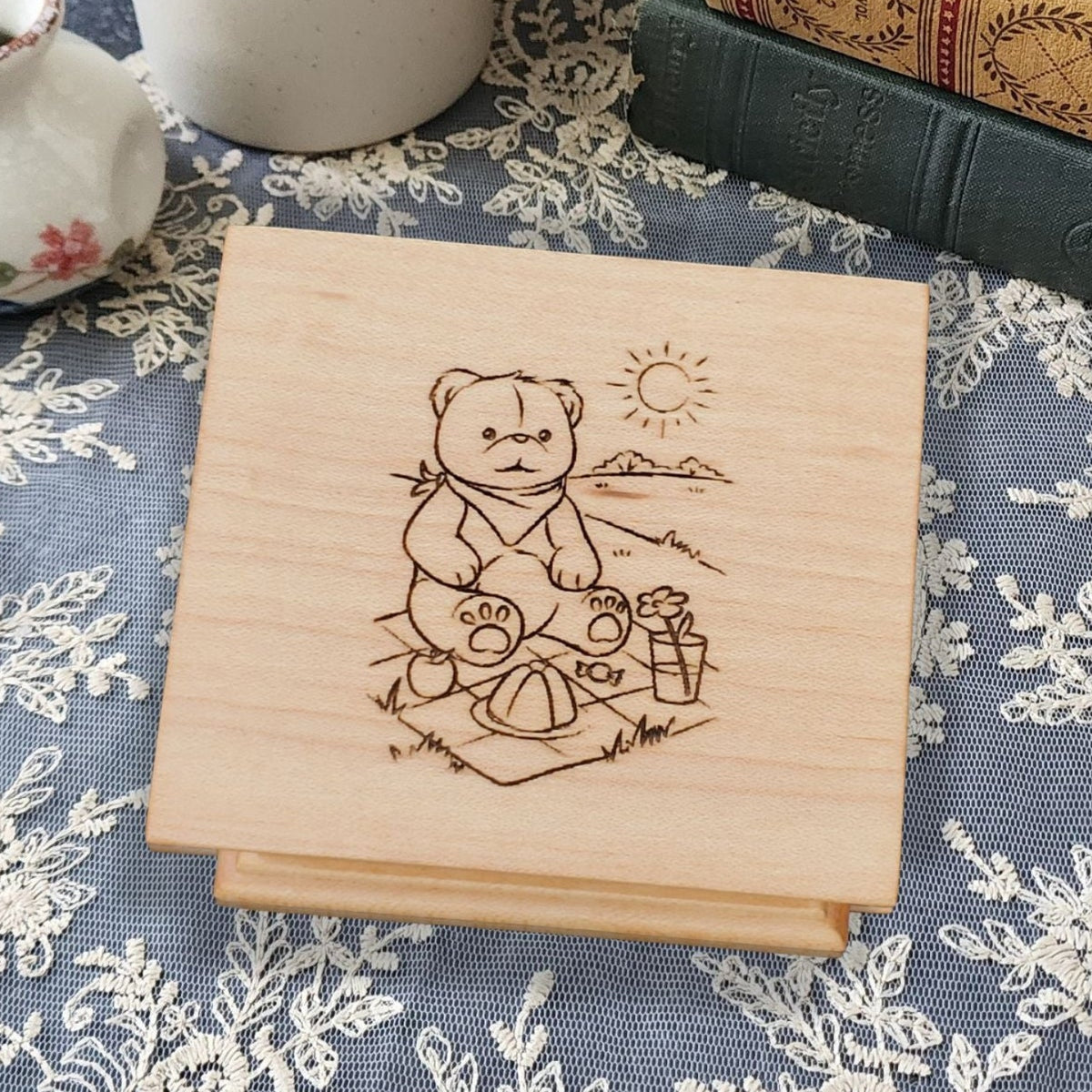 wooden music box in maple with a teddy bear sitting on a picnic blanket with mountains and sun behind him, choose song, and color, add personalized engravings