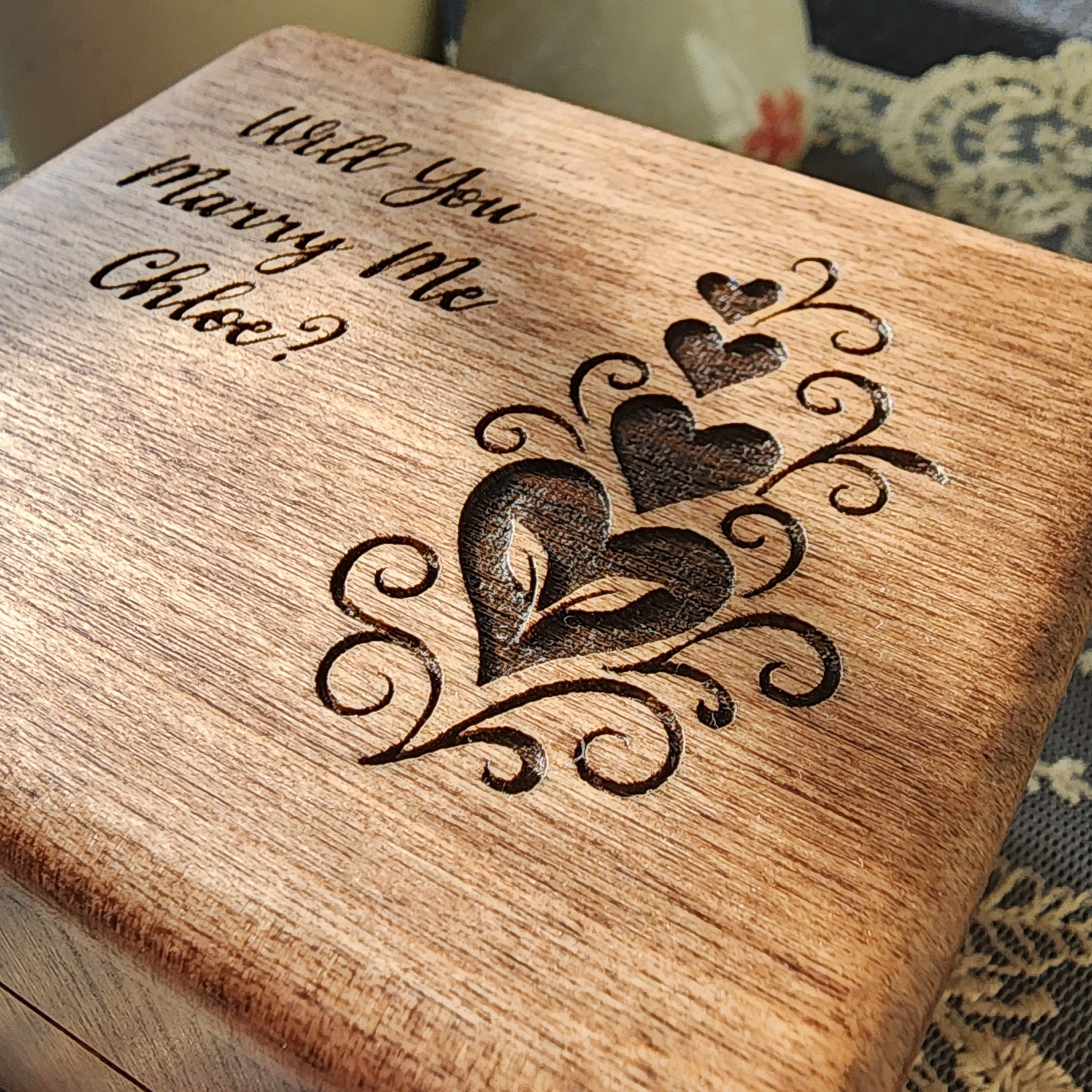 Heart Engraved Wooden ring box with engraved question 'Will you marry me Chloe?' on a textured fabric background