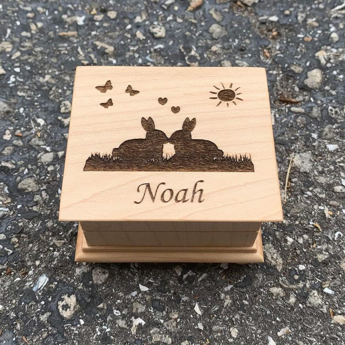 Easter theme music box with 2 kissing bunnies on the top with hearts, butterflies and a sun, with your name engraved under the image