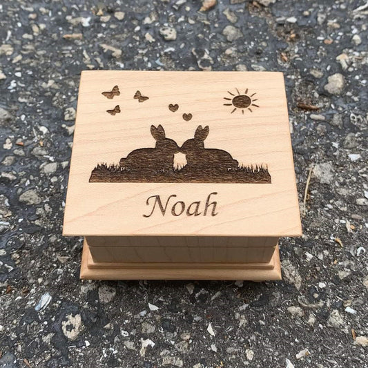 Easter theme music box with 2 kissing bunnies on the top with hearts, butterflies and a sun, with your name engraved under the image