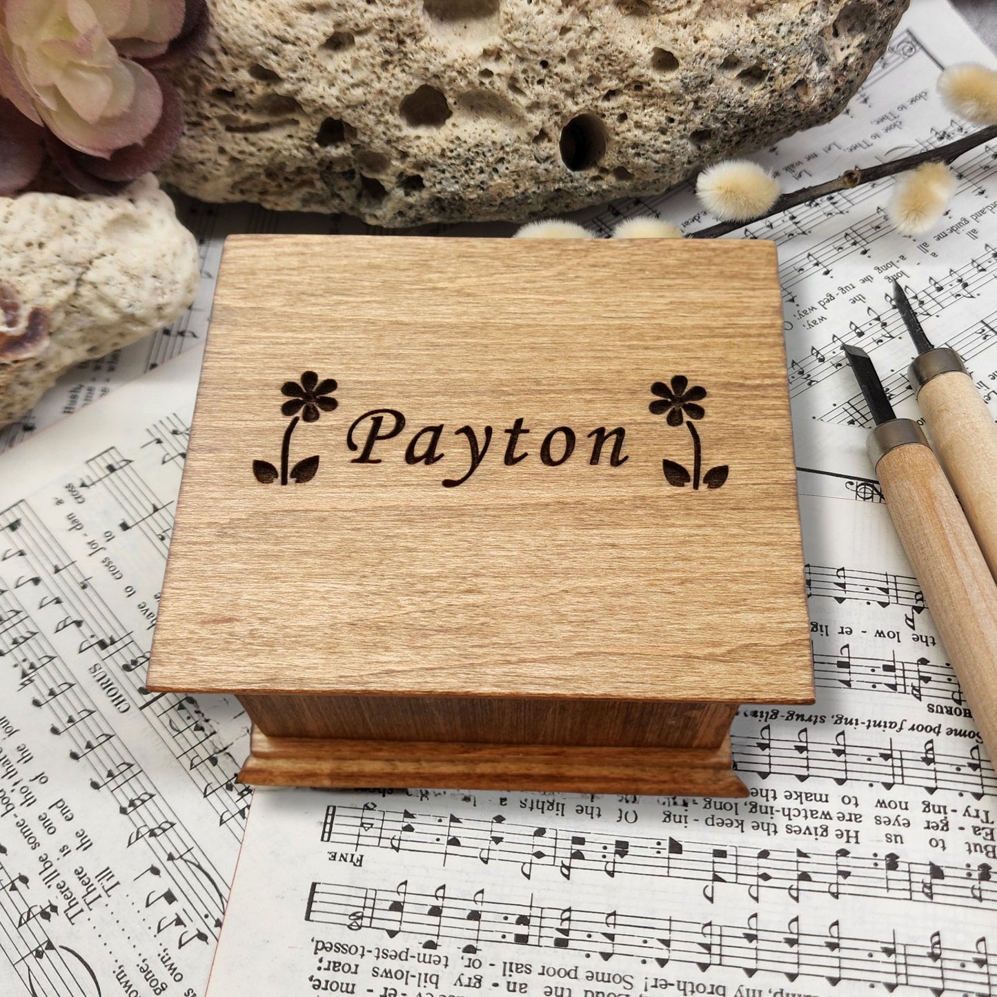 Wooden music box with 'Payton' and 2 daisies engraved on sheet music with a rock and tool in the background