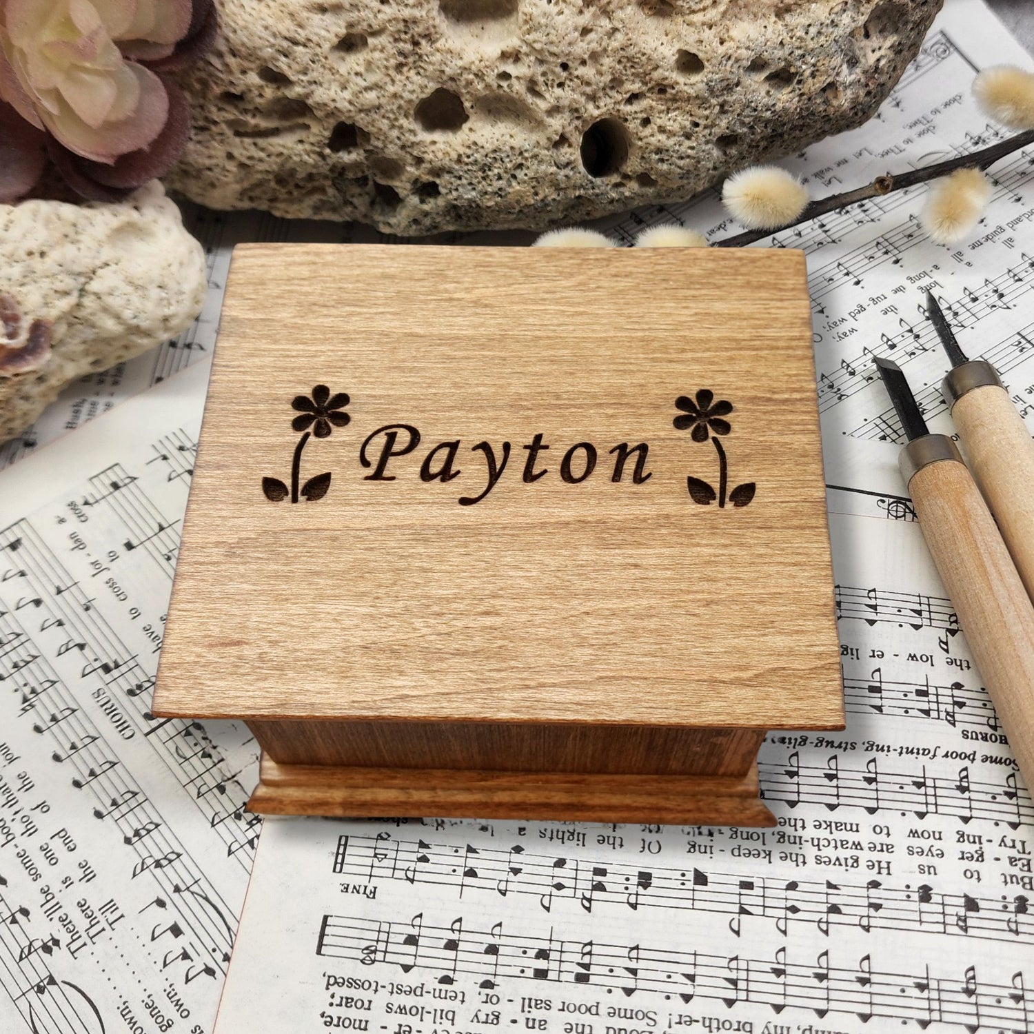 Wooden music box with 'Payton' and 2 daisies engraved on sheet music with a rock and tool in the background