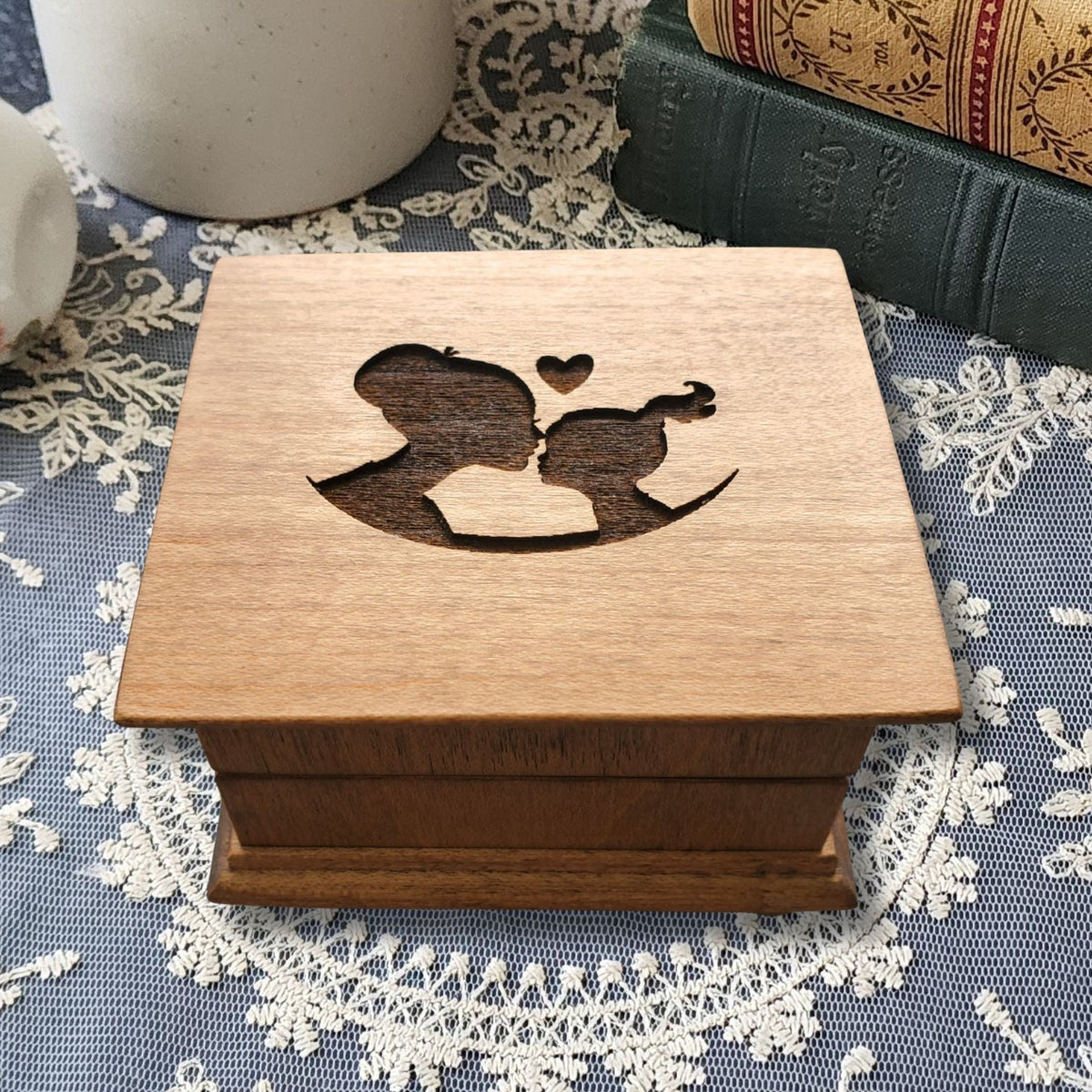 Wooden music box engraved with a mother-daughter silhouette design on a lace tablecloth