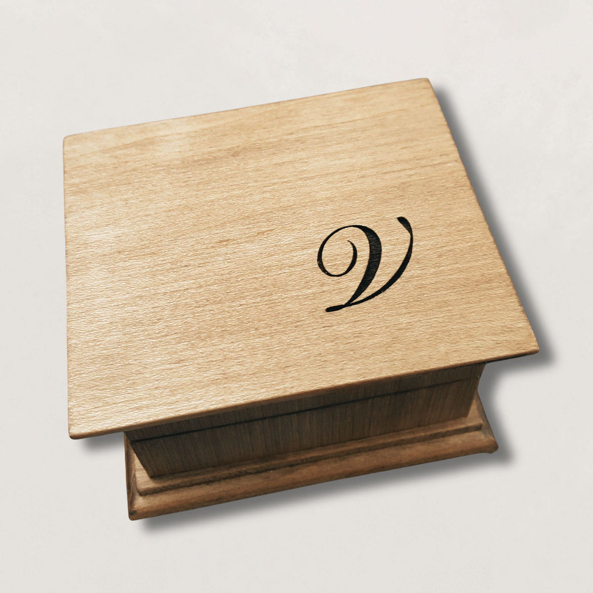 Wooden music box with a monogram 'V' engraved on the top, on a light gray background