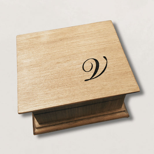 Wooden music box with a monogram 'V' engraved on the top, on a light gray background