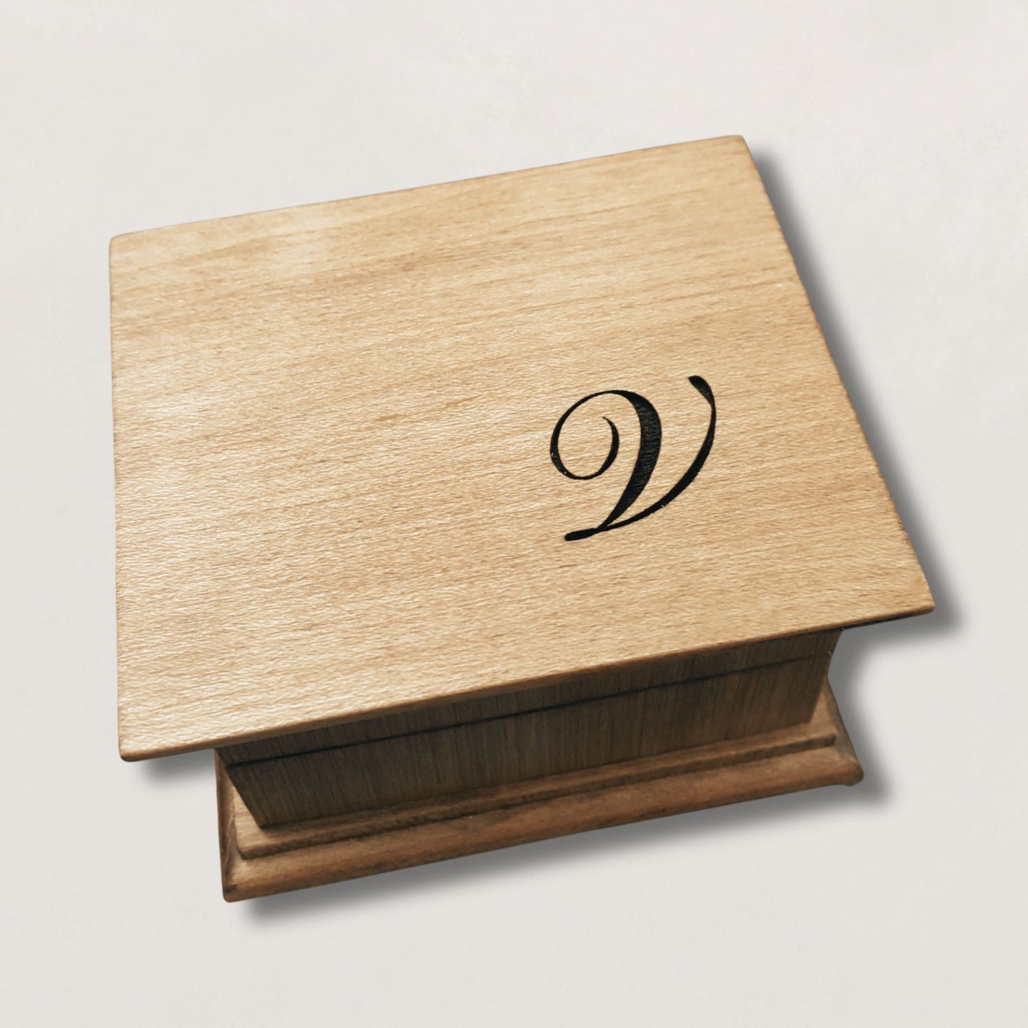 Wooden music box with a monogram 'V' engraved on the top, on a light gray background