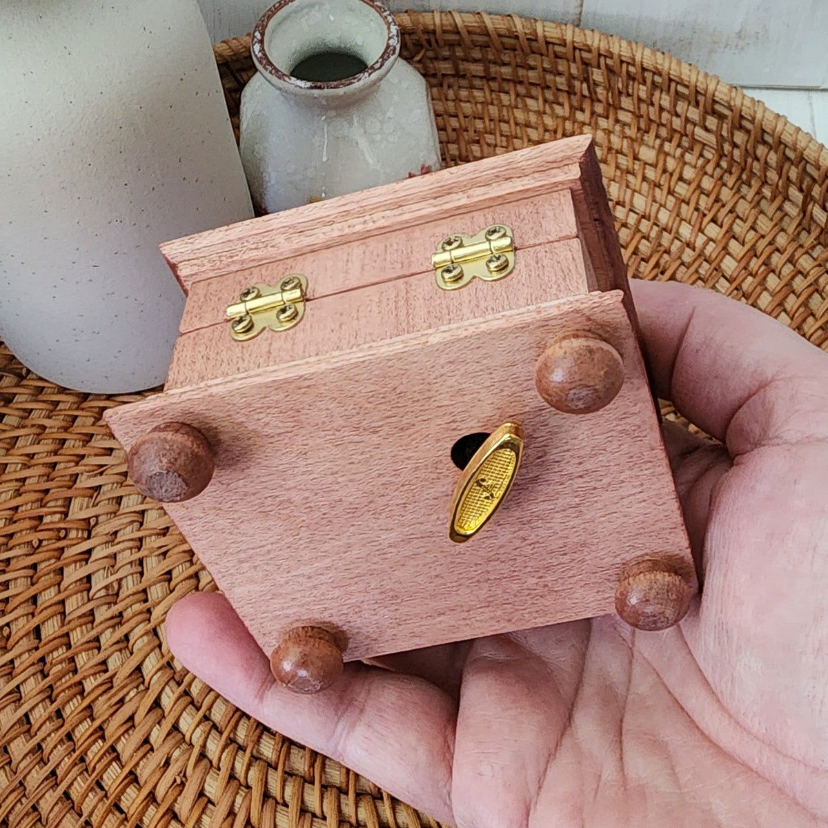 Hand holding a wooden music box with a golden wind up key on the bottom side 