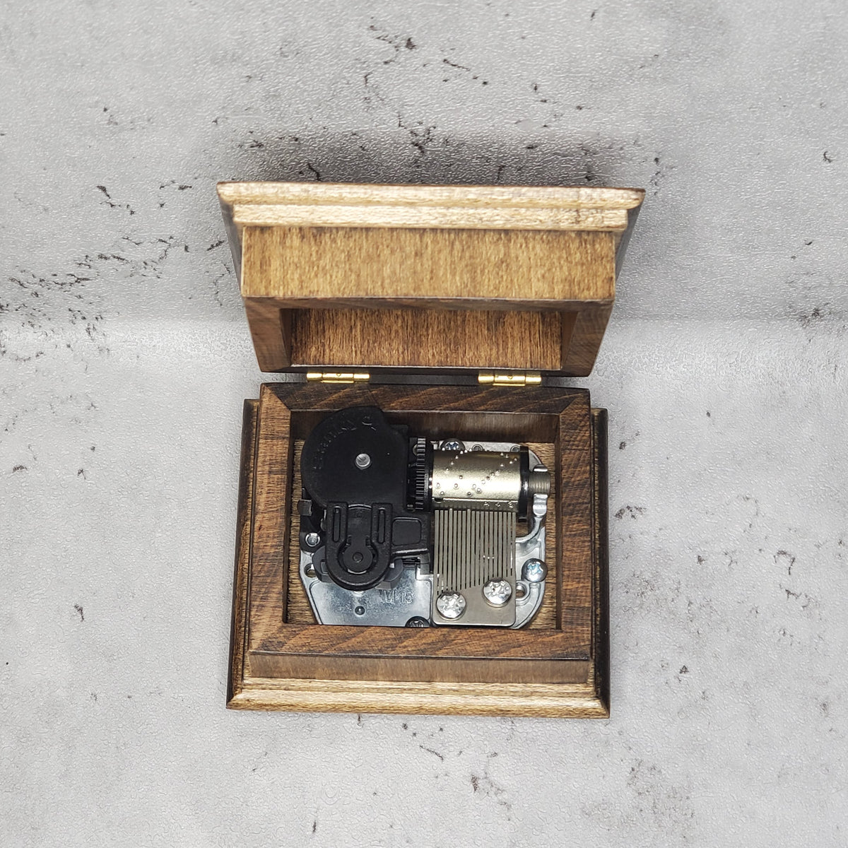 Wooden music box with a mechanical music player on a gray concrete surface