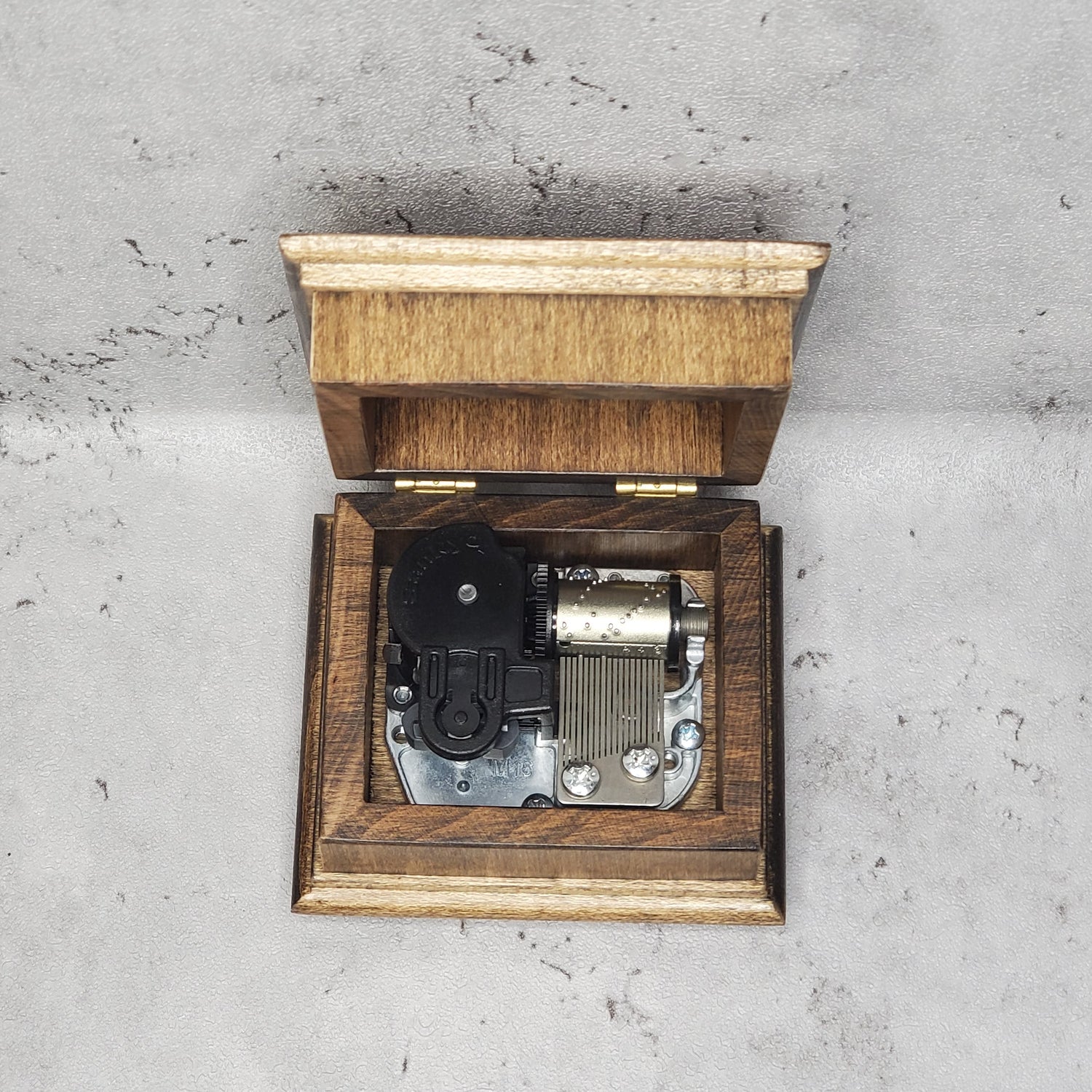 Wooden music box with a mechanical music player on a gray concrete surface