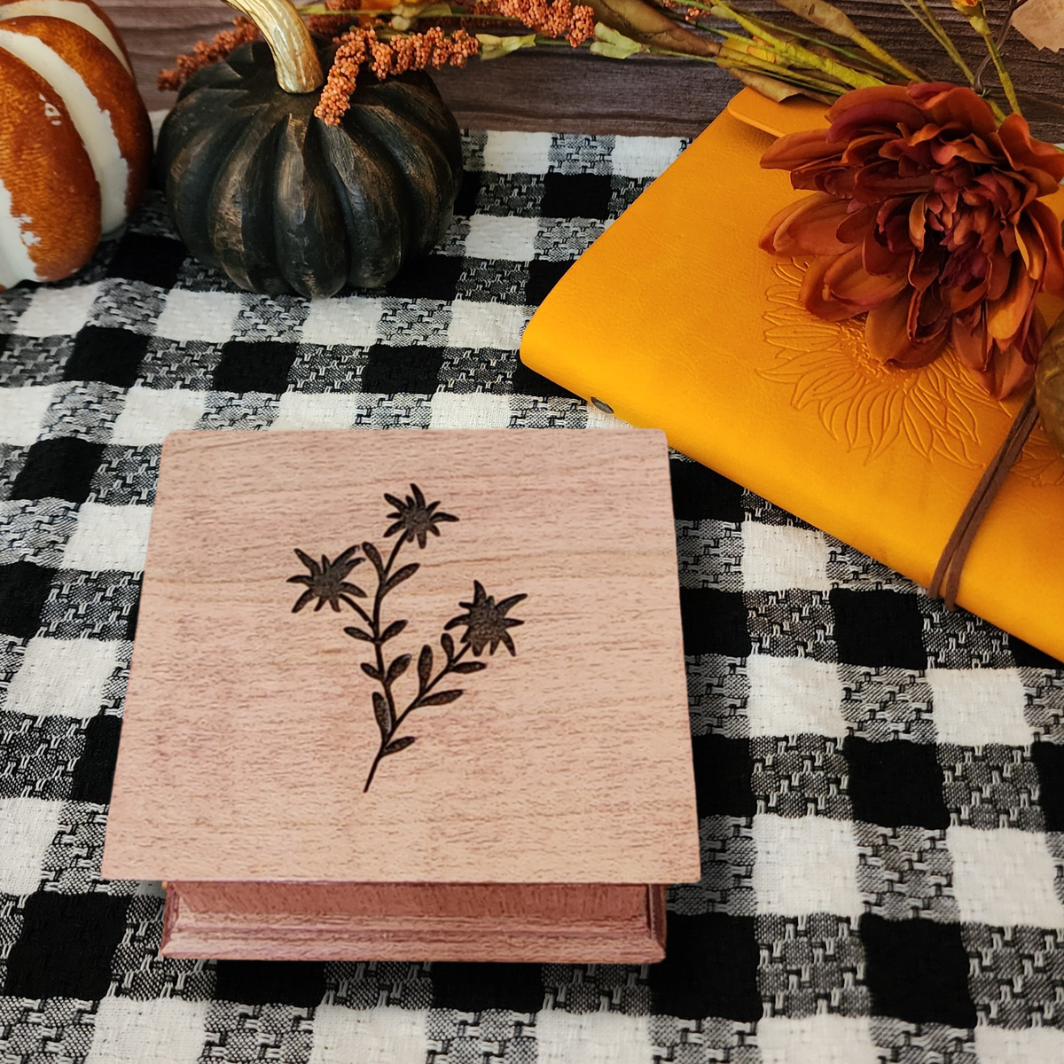 Wooden music box with floral design on a checkered tablecloth with pumpkins and flowers.